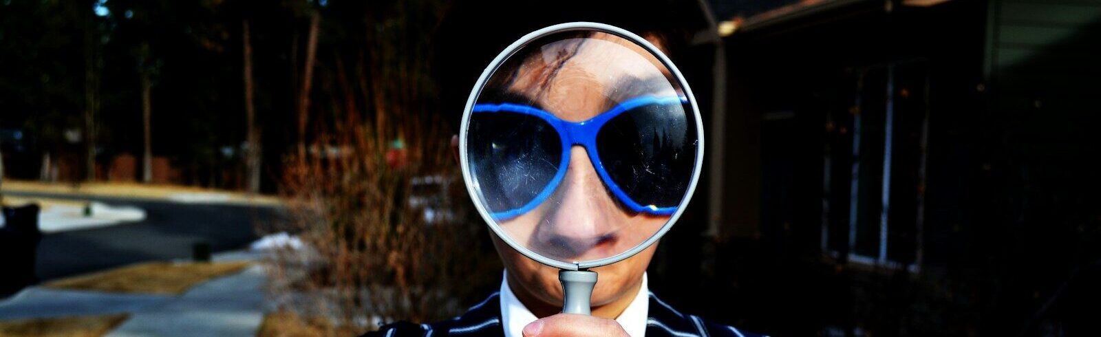 person using magnifying glass enlarging the appearance of his nose and sunglasses